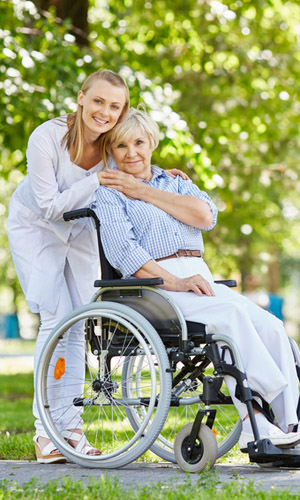 Young female in uniform with senior patient in a wheelchair chilling out in park